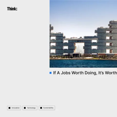 A modern, horizontally-segmented building sits by the water. The structure is composed of stacked rectangular blocks. 