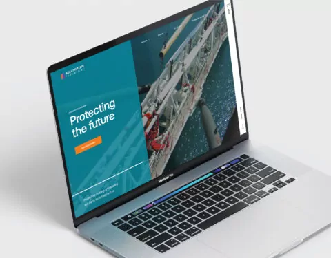 A laptop displays a website; it shows a teal background with the words “Protecting the future” and an image of offshore oil rig equipment.