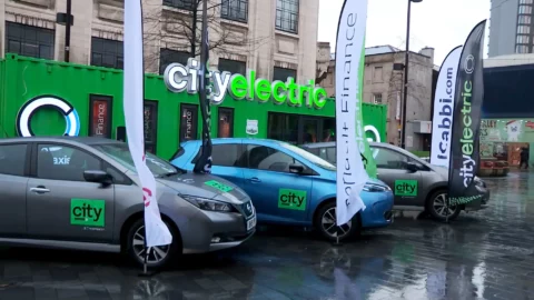 Three City Taxis cars are parked in a row with a large white and green sign saying 'city electric' behind
