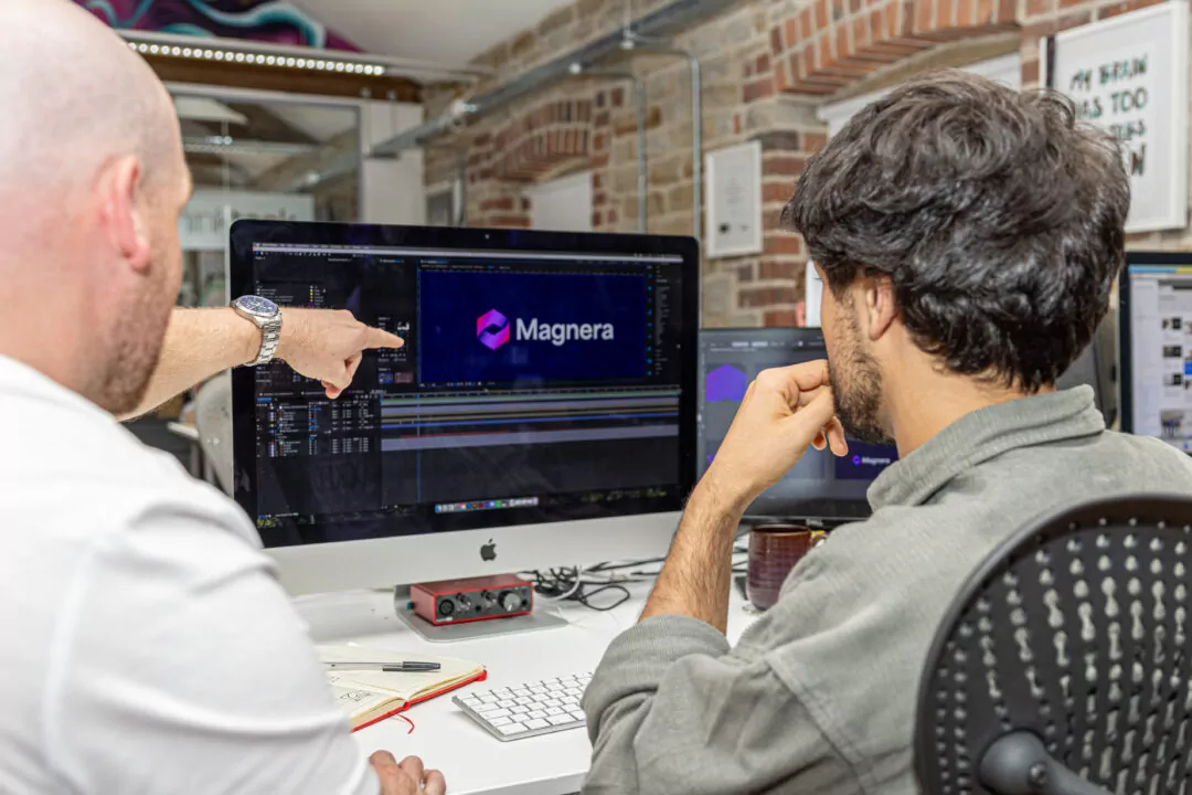 Joe and Amin look at a computer screen displaying the Magnera logo within video editing software.