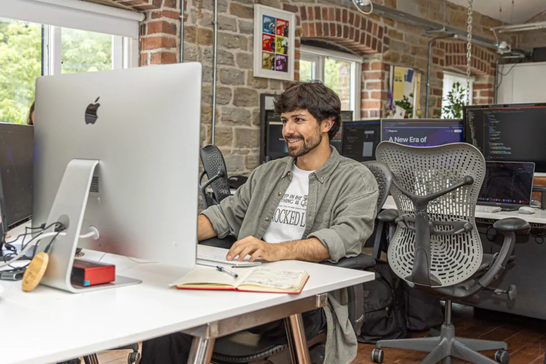 Amin smiling while seated at a desk in a modern, brick-walled office.