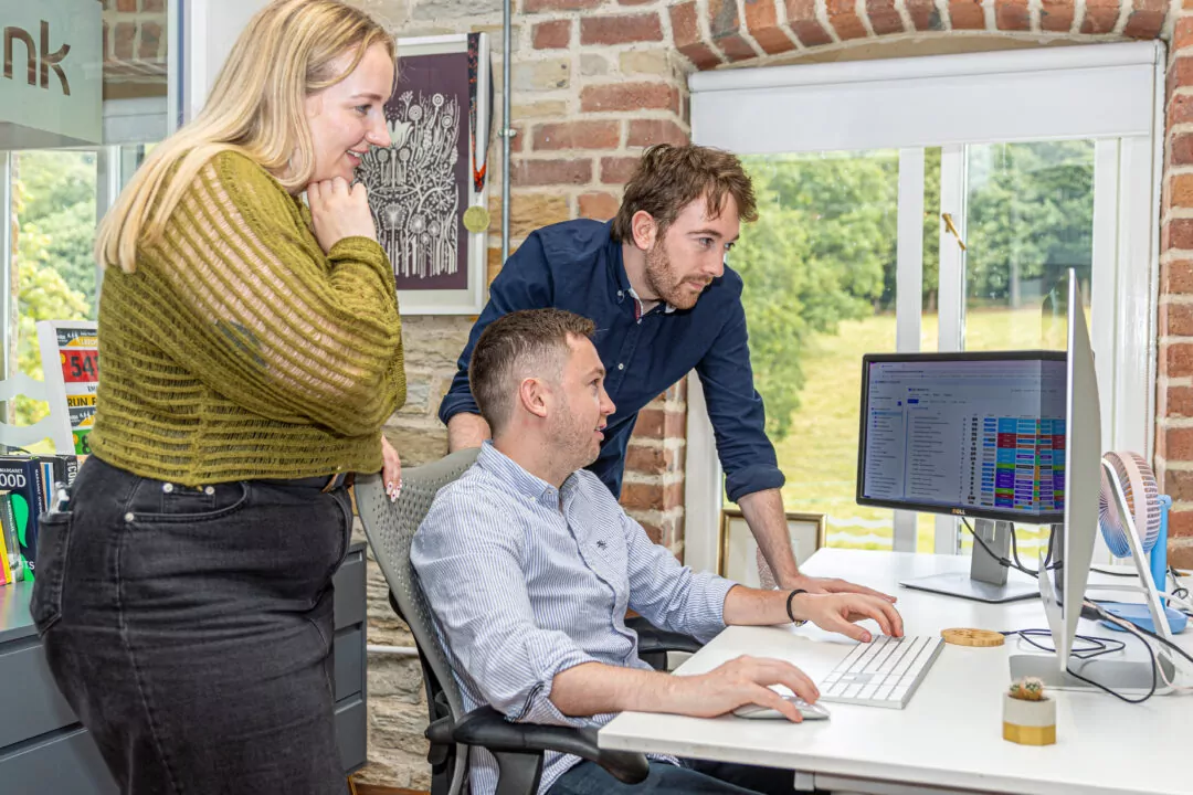 Chloe Arnett, Thomas Smith and Dr. Nathan Hunt looking at two computer screens on a white desk.