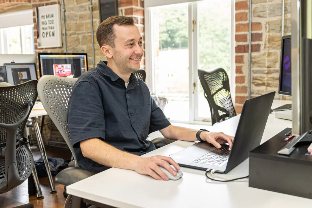 Paul, a member of the web development team, using a laptop; he is seated at a white desk in a contemporary office.