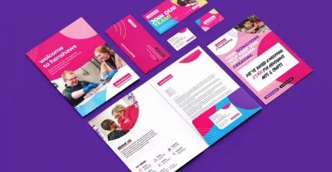 Brochures, business cards, and a letterhead, displaying vibrant pink and teal designs, are arranged on a purple background. Text includes: “welcome to henshaws,” “JOIN OUR TEAM!”, and “YOUR DONATIONS HELP KEEP OUR ART MAKERS CREATING.” “WE’VE RAISED A WHOPPING £11,000 FOR ORIGINAL ARTS & CRAFTS!”