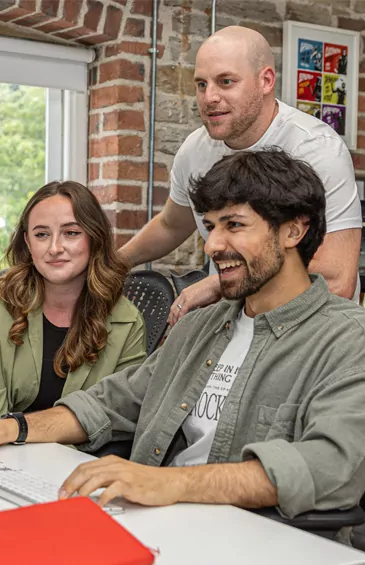 Members of the creative branding team, Emily, Joe and Amin, collaborating around a computer.
